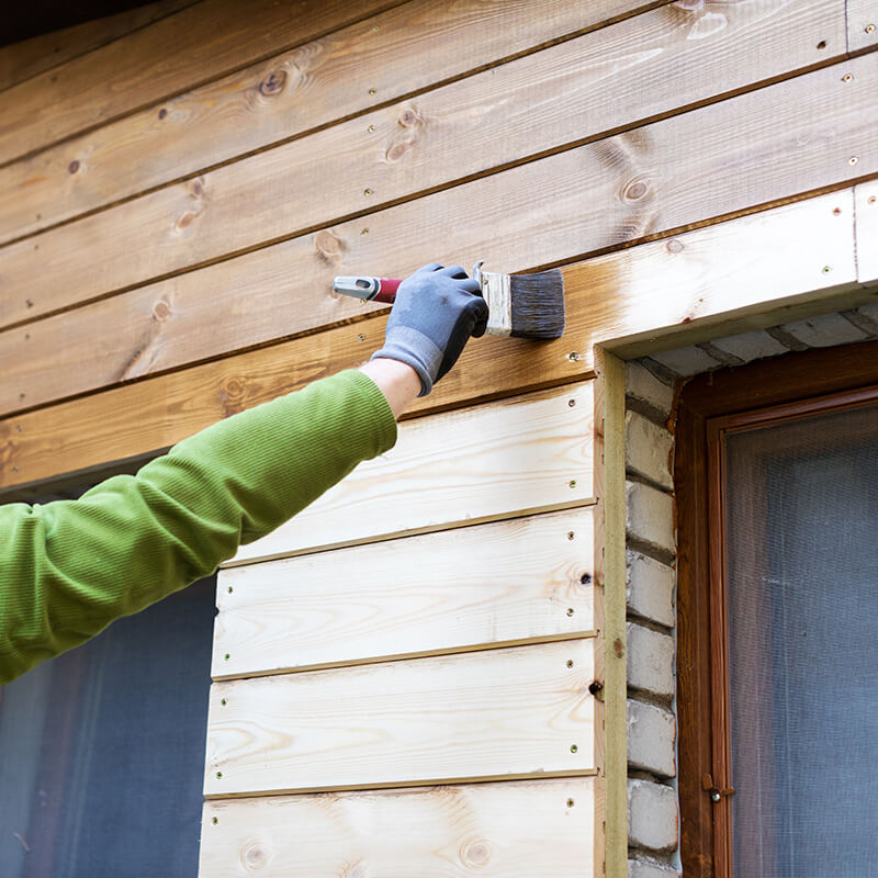 man-applying-brown-wood-oil-on-a-wooden-wall-paneling-near-windows